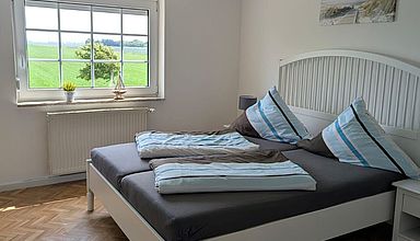 Schlafzimmer im weißen Landhaustil mit Ausblick auf grüne Wiese im Huus Fleetenkieker