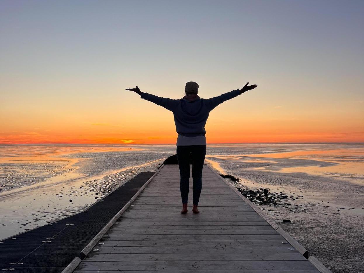 Yoga mit Imke Tamkus in der Bildmitte auf dem Steg im Trischendiek Strand vor farbenfrohem HImmel zum Sonnenuntergang