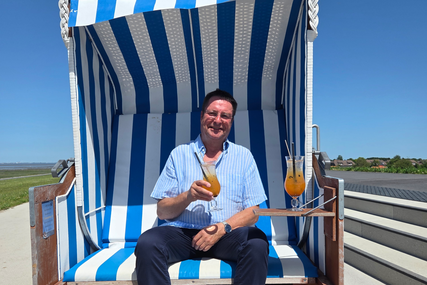 Bernd_Duncker mit seinem Trieschendiek Cocktail in der Hand im blau-weiß-gestreiften Strandkorb