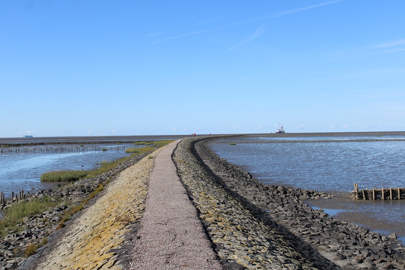 Ausblick bei blauem Himmel vom Trischendamm in Friedrichskoog auf beide Seiten des Meeres mit einem Schiff am Horiizont